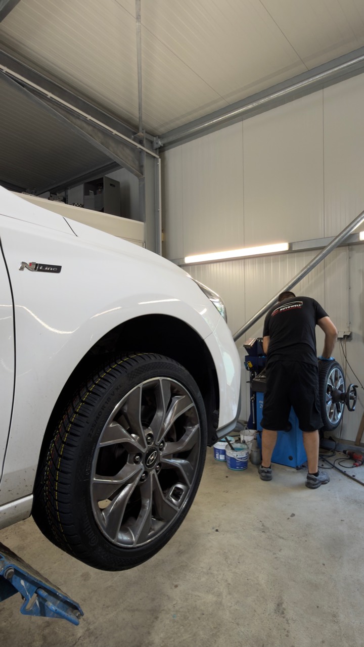 Fahrzeug auf der Hebebühne und Mitarbeiter an der Auswuchtmaschine in unserer Werkstatt